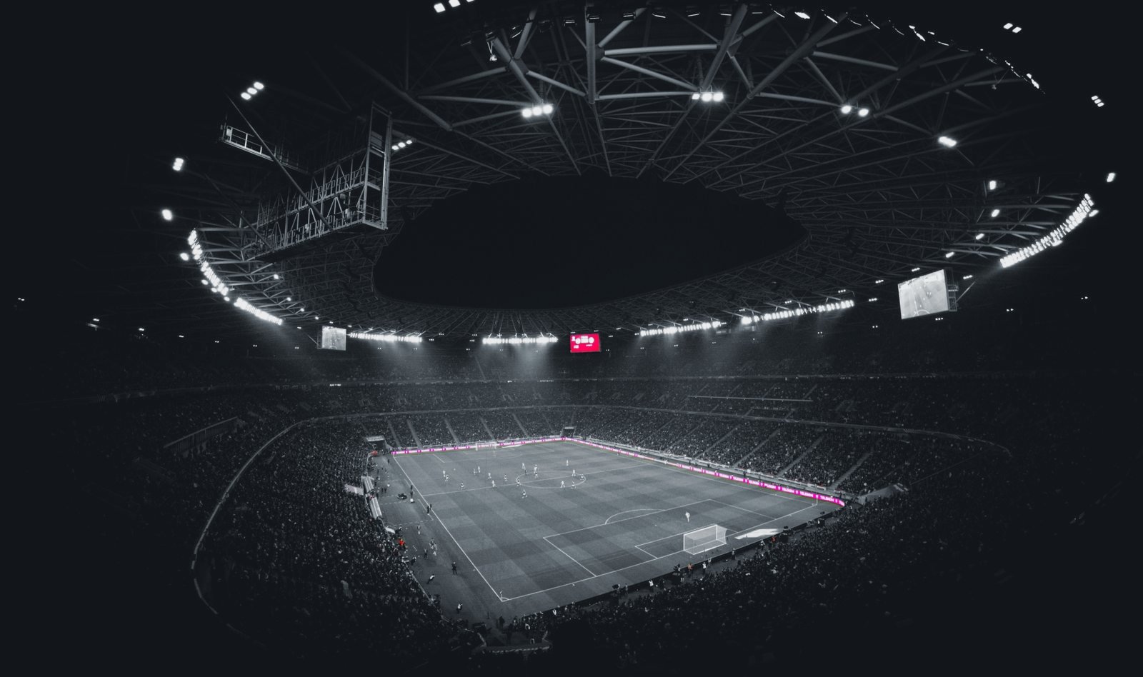 Vol voetbalstadion bij avond; de LED-reclameborden rond het veld zijn in kleur, de rest van het beeld in groen